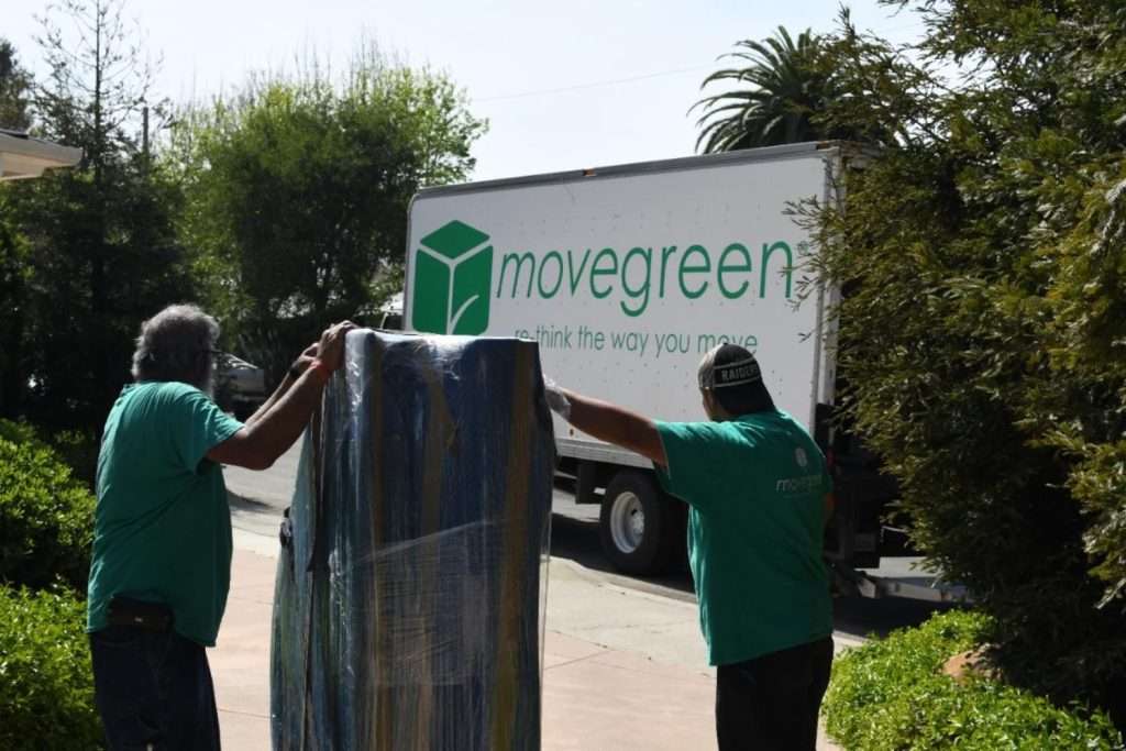 Two Movegreen team members carrying wrapped furniture out to truck